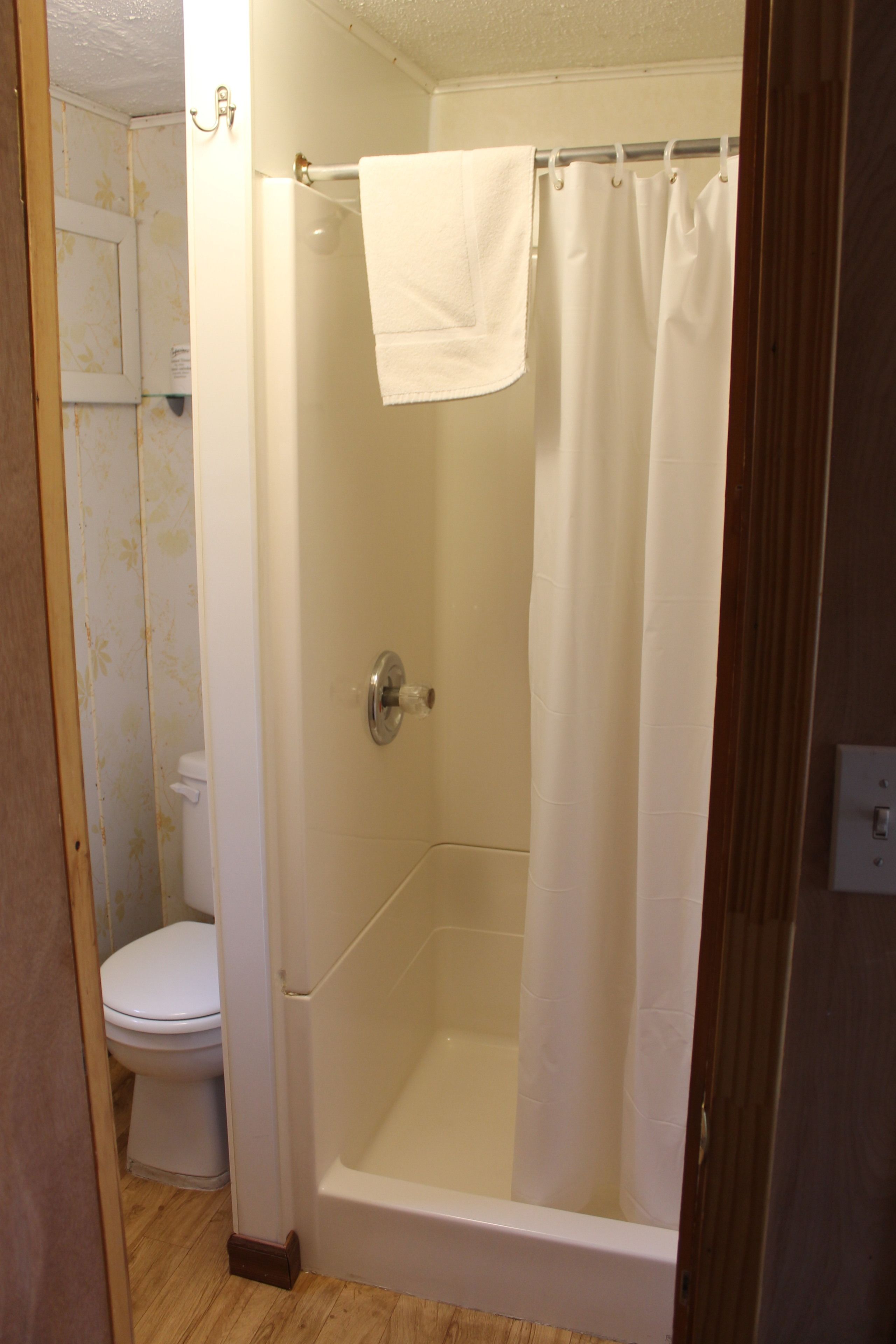 A bathroom with a shower, toilet, and a towel hanging on the shower door.