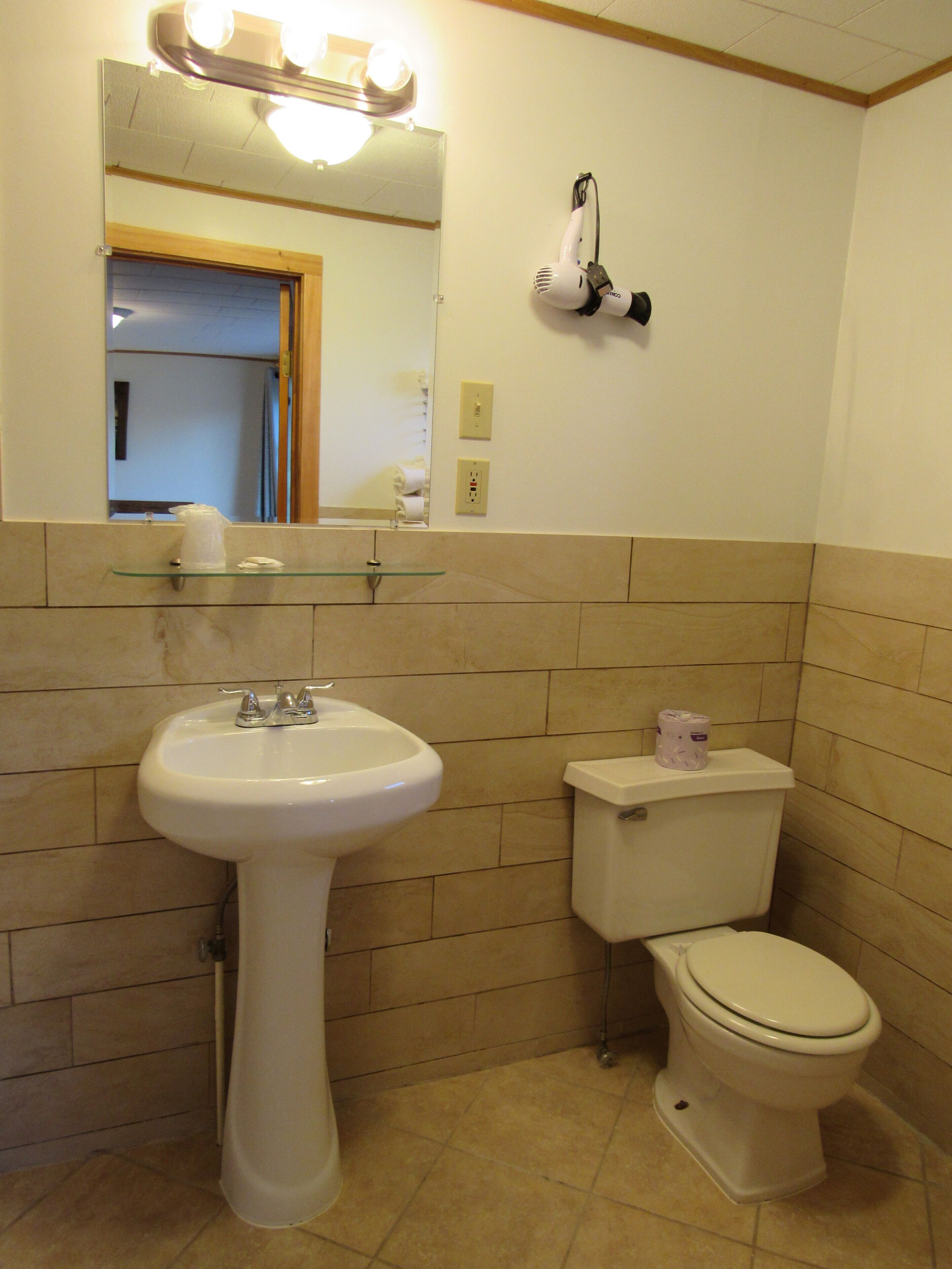 Ein Badezimmer mit einem Standwaschbecken, einer Toilette und einem Spiegel mit Beleuchtung darüber.