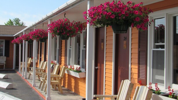 A row of motel rooms with wooden shutters, outdoor seating, and hanging flower baskets. - Acadia Gateway Motel (Trenton)
