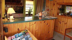 A wooden reception desk with a lamp, a plant, and various items on the counter. - Acadia Gateway Motel (Trenton)