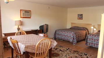 A room with a dining table, two beds with patterned bedding, a television, and a wall-mounted air conditioner.