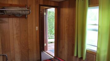 A room with wooden paneling, a bed with a patterned bedspread, a metal rack, and a window with green curtains.