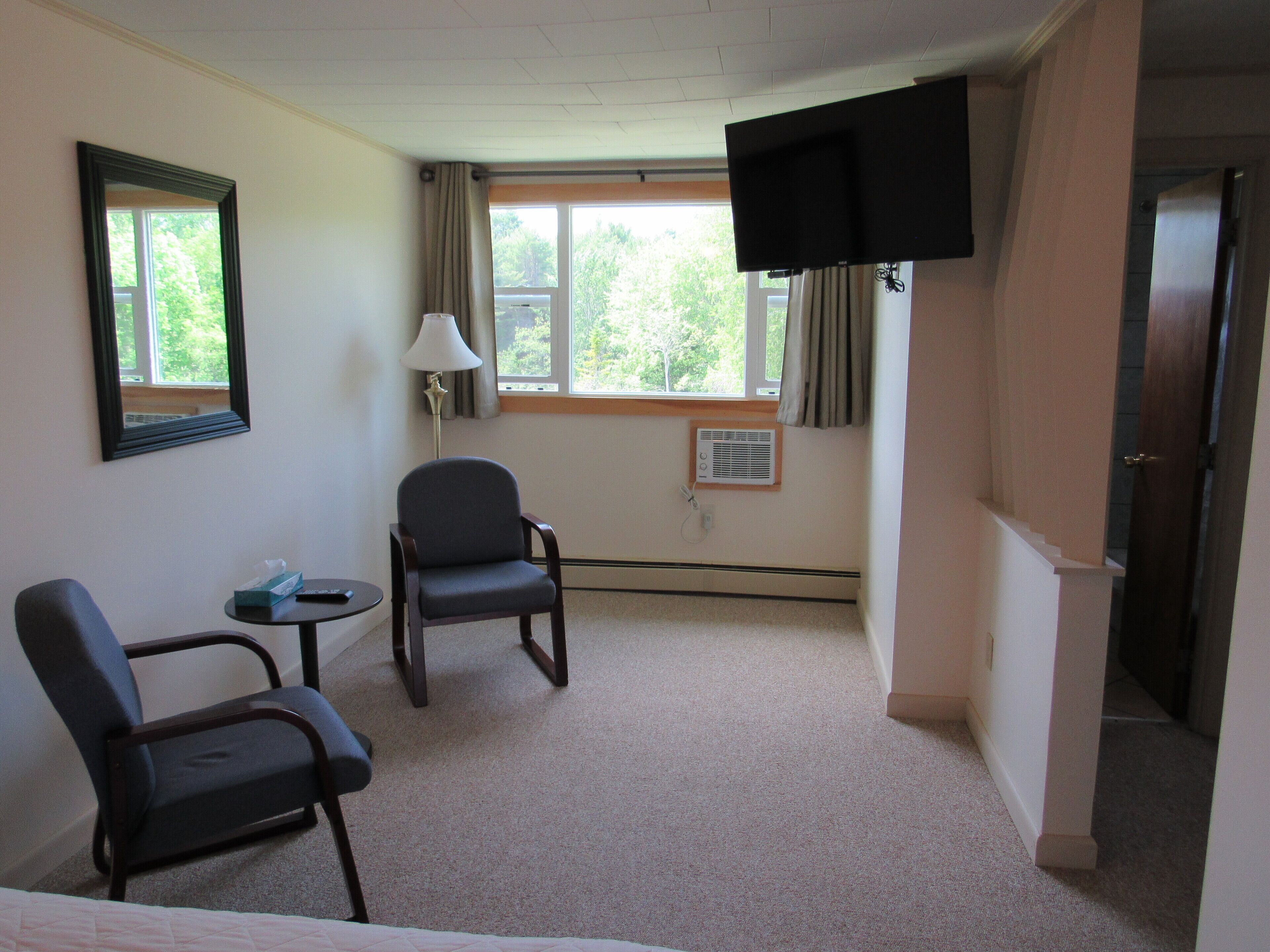 A hotel room with two chairs, a TV, a lamp, and a window with curtains.
