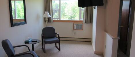 A hotel room with two chairs, a TV, a lamp, and a window with curtains.