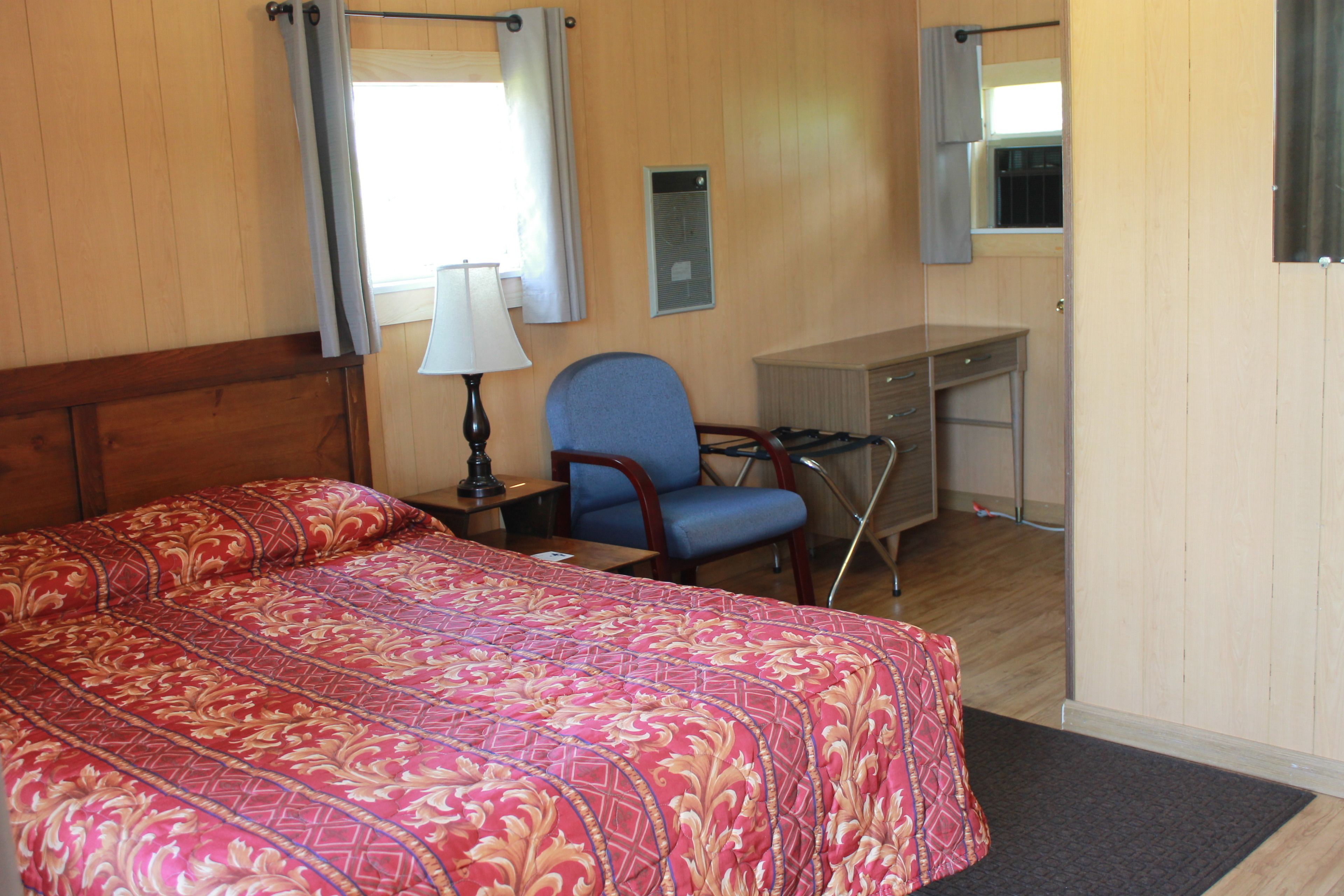 Ein Hotelzimmer mit einem großen Bett, einem Schreibtisch, einem Sessel und einem Fenster mit Vorhängen.