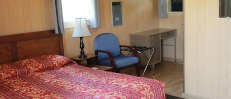 Ein Hotelzimmer mit einem großen Bett, einem Schreibtisch, einem Sessel und einem Fenster mit Vorhängen.