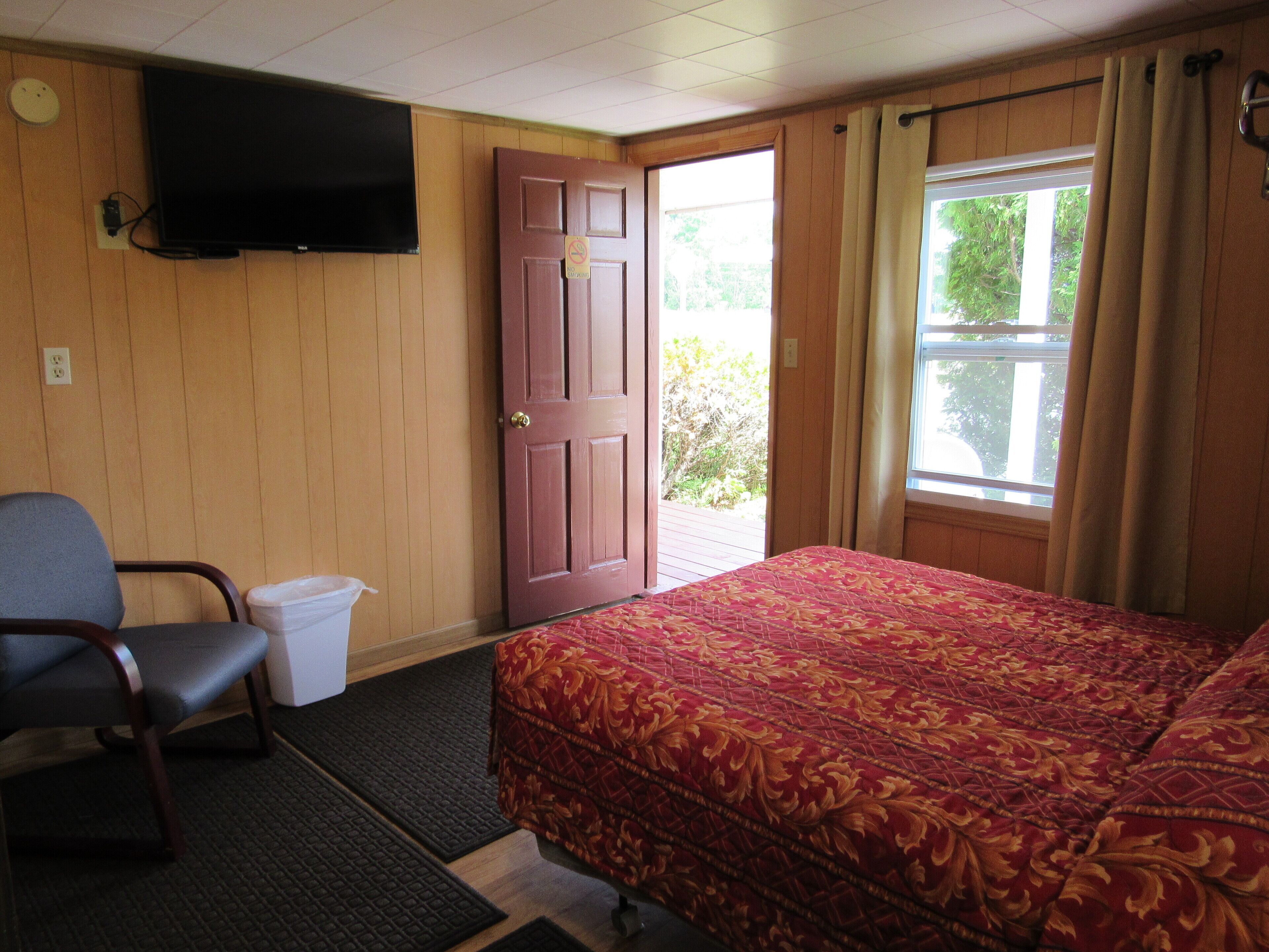 A room with a bed, a chair, a television mounted on the wall, a door, and a window with curtains.