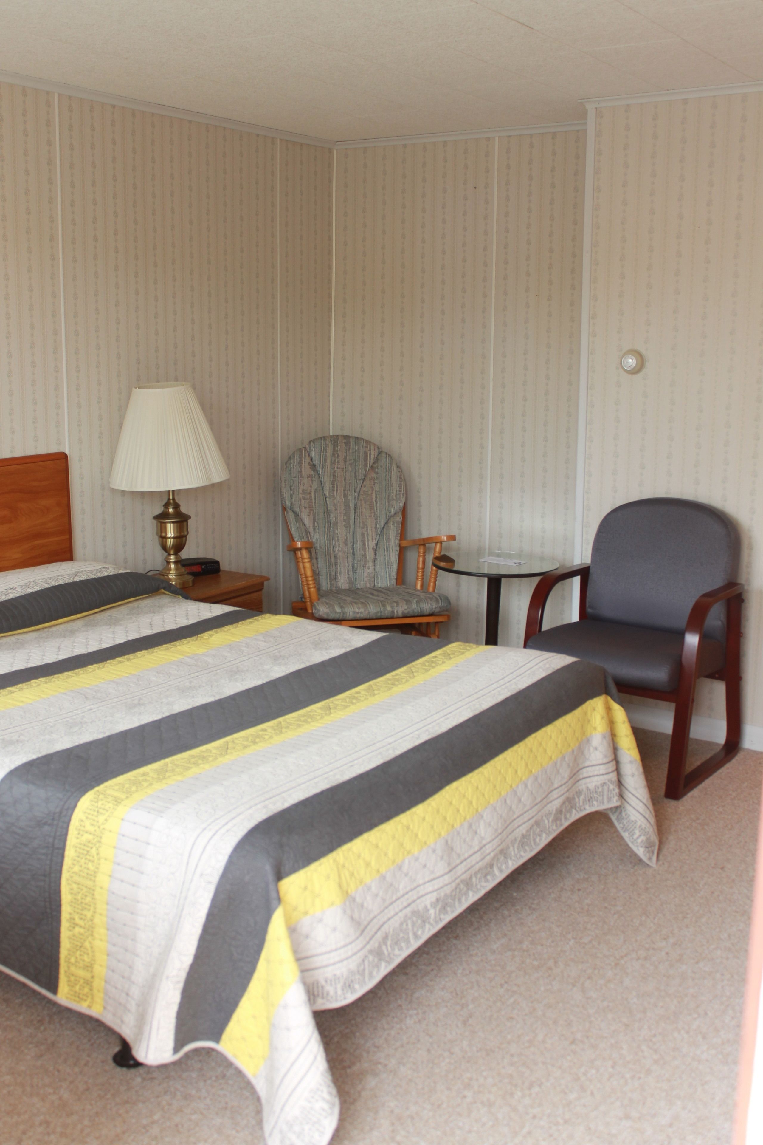 A hotel room with a large bed, two armchairs, a small table, and a lamp.