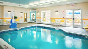 An indoor swimming pool with clear water, yellow lounge chairs, and a visible exit sign.