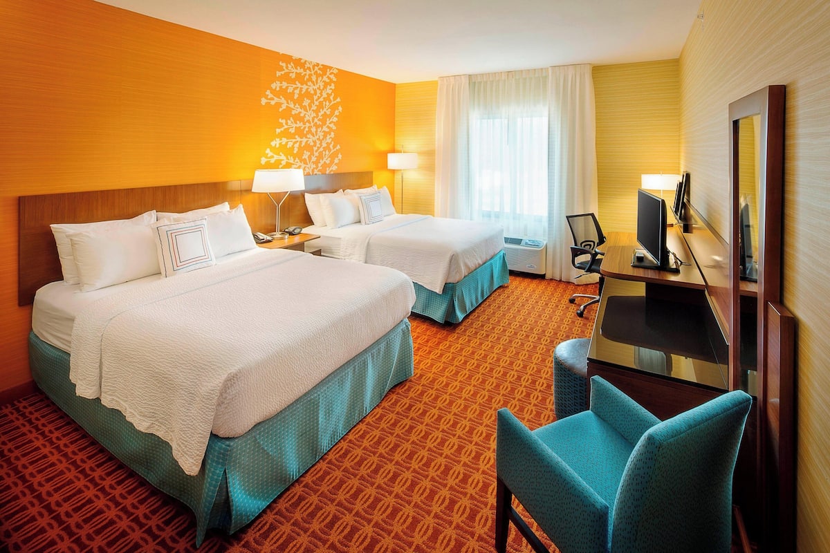 A hotel room with two beds, a desk with a computer, a chair, and a large mirror.