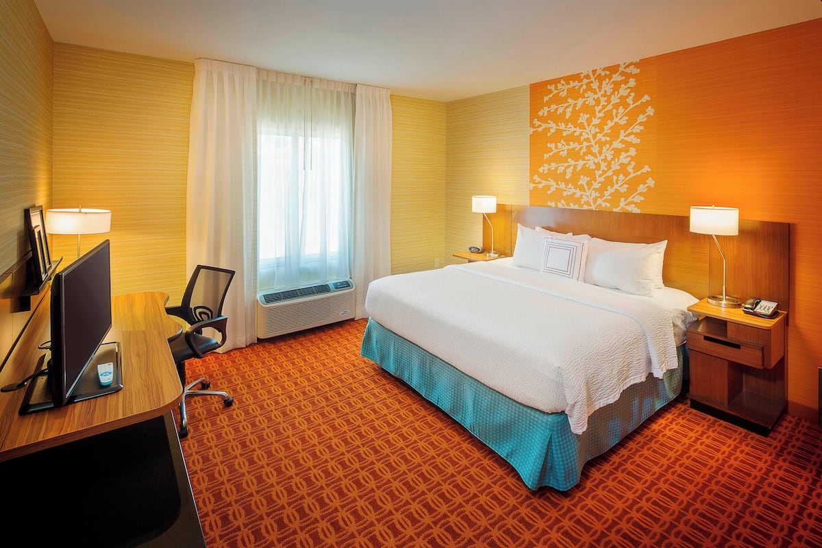 A hotel room with a large bed, two bedside tables with lamps, a desk with a computer, and a window with curtains.
