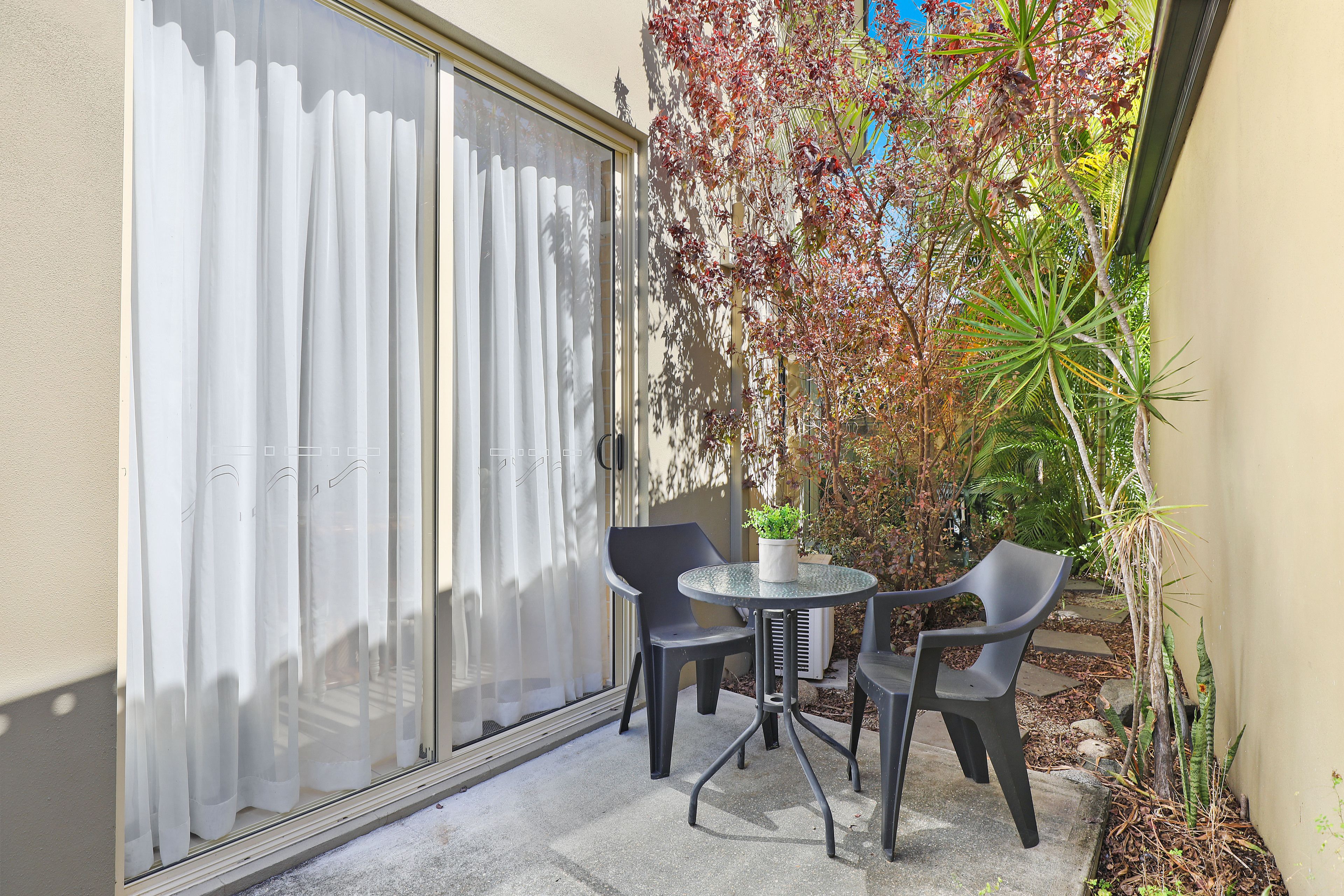 A patio with a table and chairs, a potted plant, and a sliding glass door.