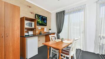 A compact kitchen with a microwave, toaster, and a TV on the wall. There is a dining table with chairs and a window with curtains.