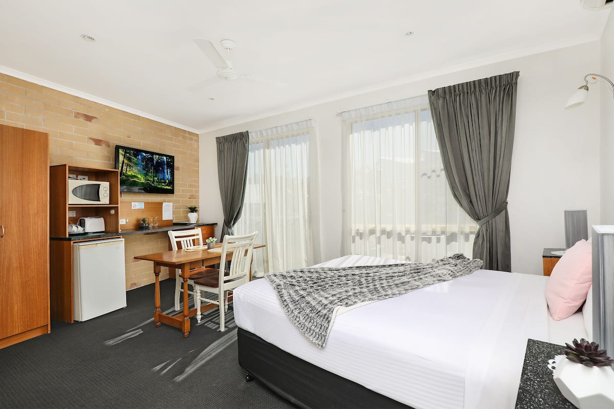 A hotel room with a bed, a desk with a microwave, a TV, and a small refrigerator.