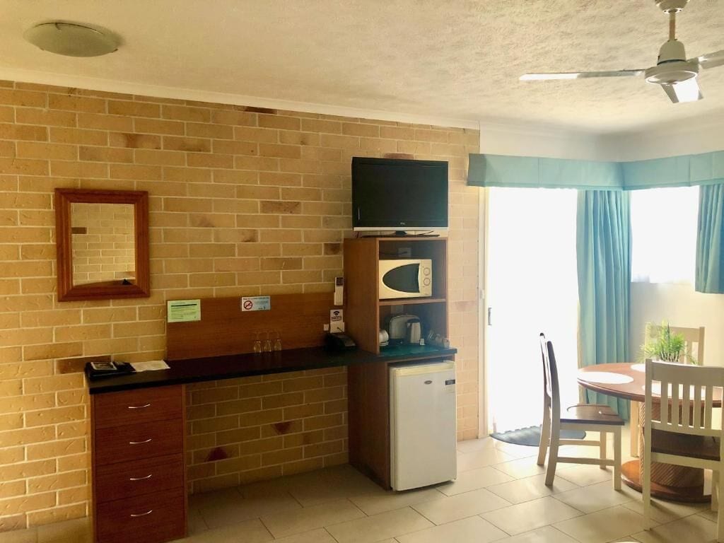 A compact kitchen with a refrigerator, microwave, and a flat-screen TV on a wooden stand.