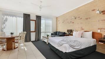Una habitación de hotel moderna con una cama grande, una mesa de comedor con sillas, un sofá y una pared decorativa de ladrillo.