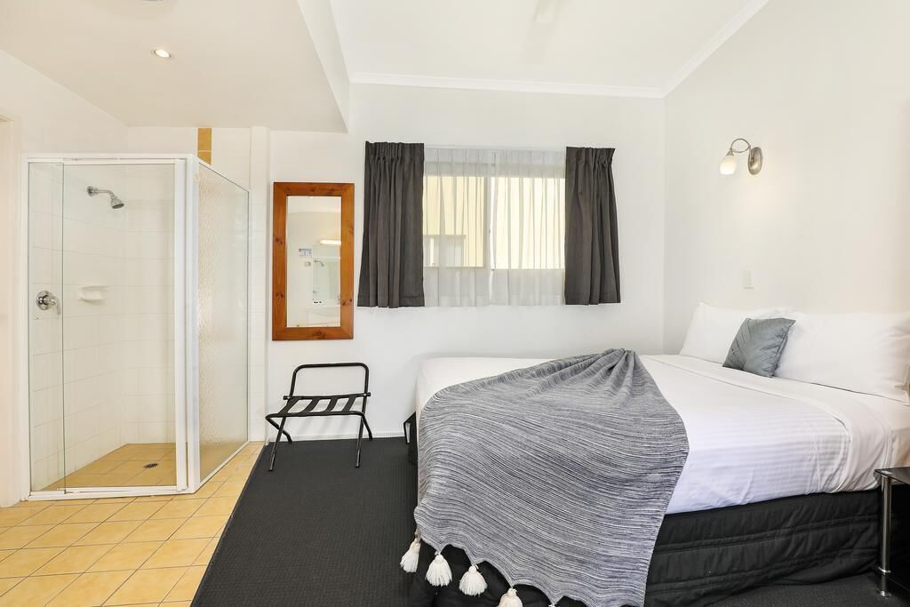 A hotel room with a bed, a shower, a chair, and a window with curtains.