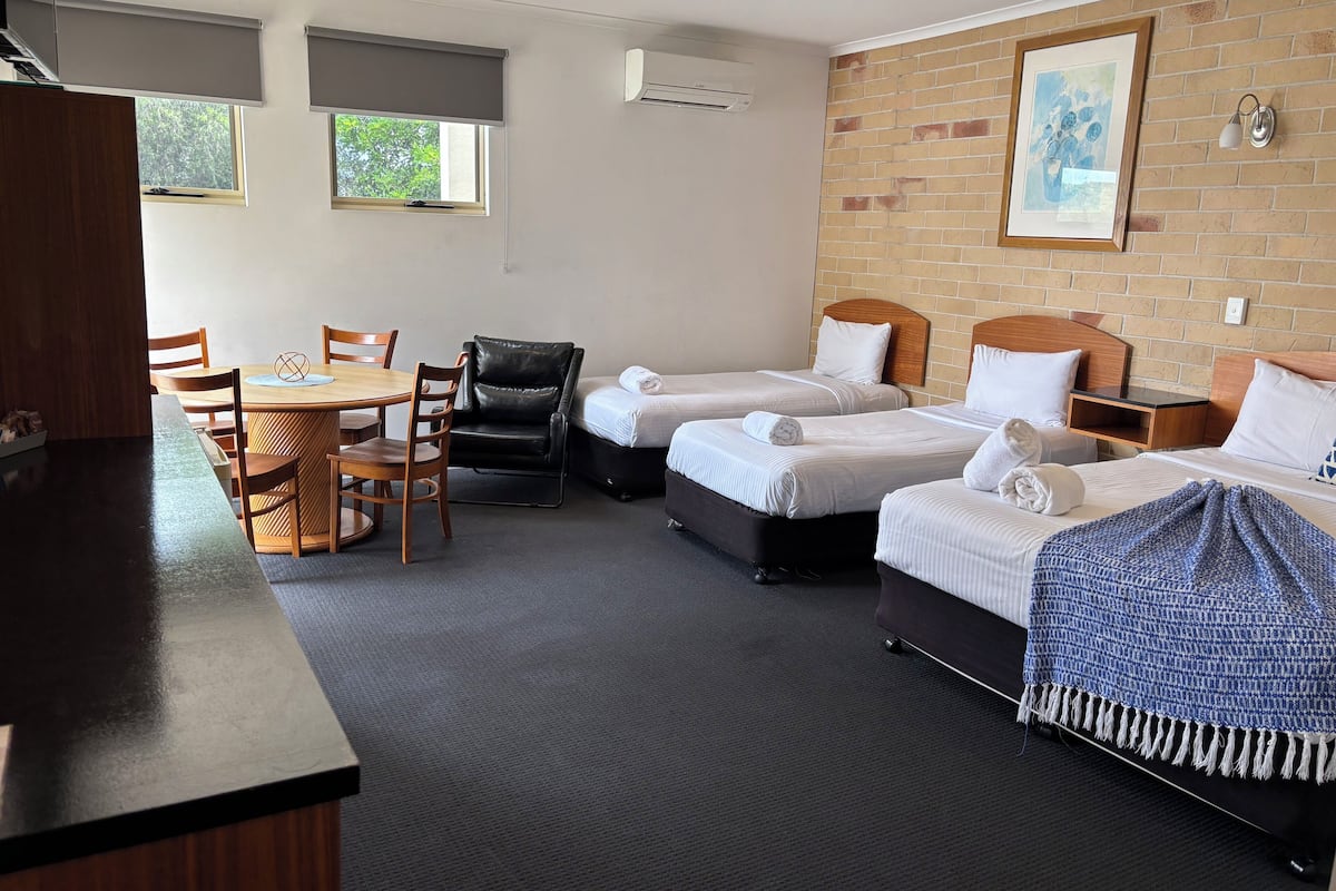 A hotel room with two beds, a desk with a chair, a small table, and a brick wall with a picture.