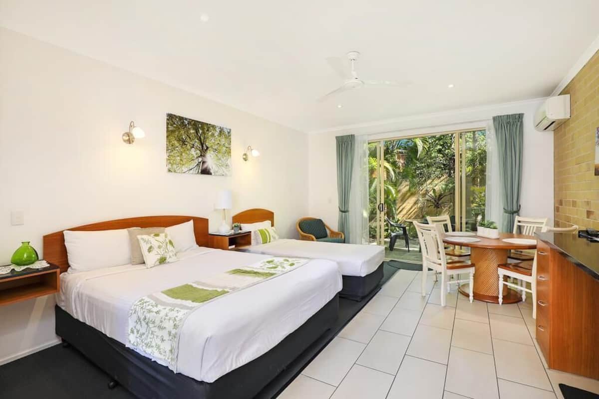 A hotel room with two beds, a dining area, and a view of the outdoors.
