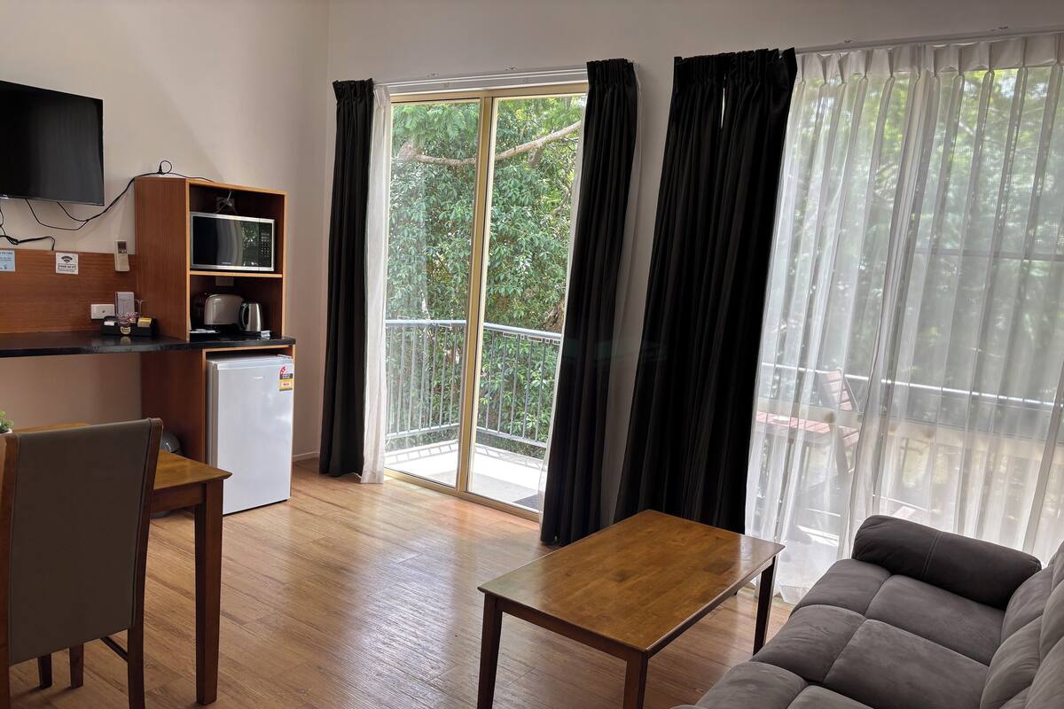 A modern living room with a sofa, a dining table, and a kitchen area with a refrigerator and microwave.