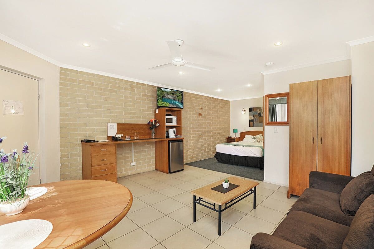 A compact hotel room with a kitchenette, a dining area, a sofa, and a bed.