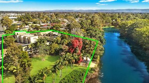 Vista aérea de una zona residencial con casas, un río y un espacio verde con palmeras.