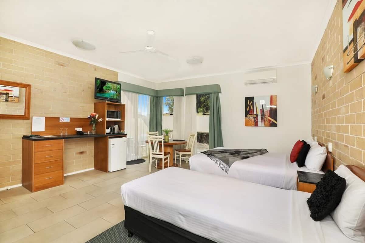 A hotel room with two beds, a kitchenette, a TV, and a dining area.