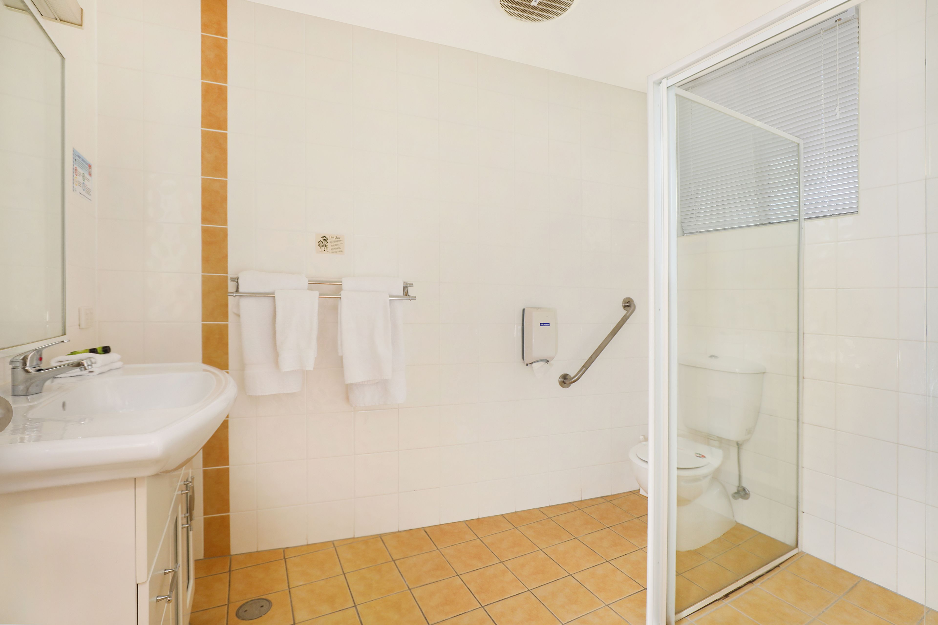 Un baño con lavabo, azulejos blancos, cabina de ducha de cristal y retrete.