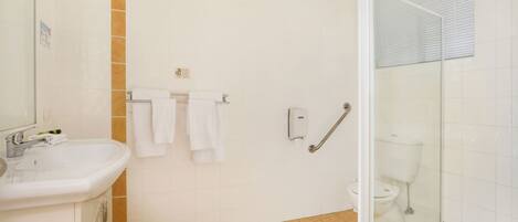 Un baño con lavabo, azulejos blancos, cabina de ducha de cristal y retrete.