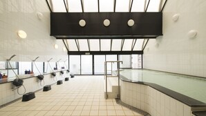 A modern indoor swimming pool with a tiled floor, multiple showerheads, and a glass ceiling.