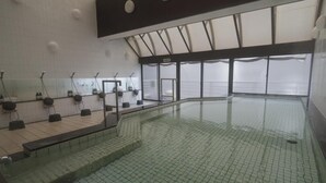 A swimming pool with tiled flooring, a glass barrier, and a ceiling with a grid pattern.