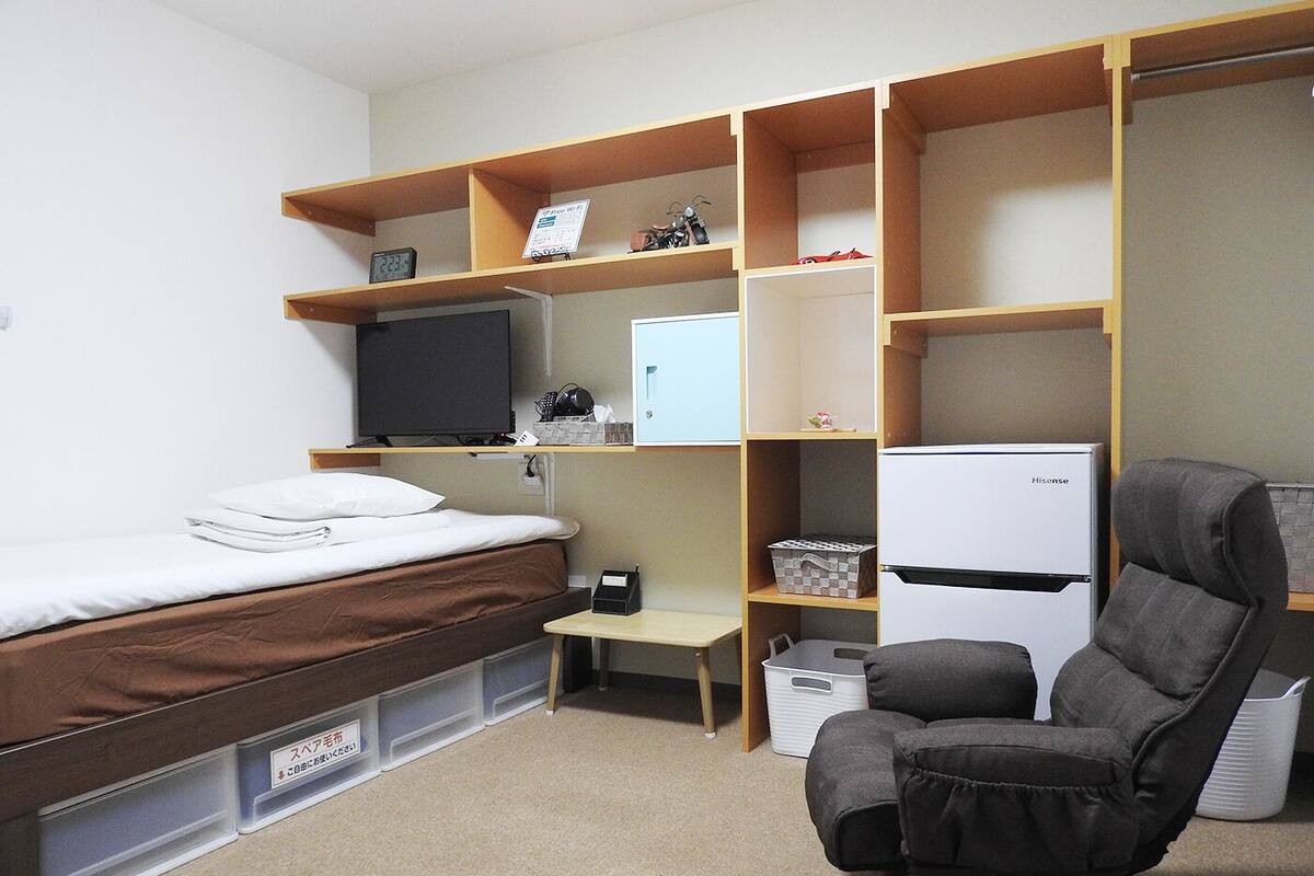 A compact hotel room with a bed, a desk, a chair, a television, and a refrigerator.