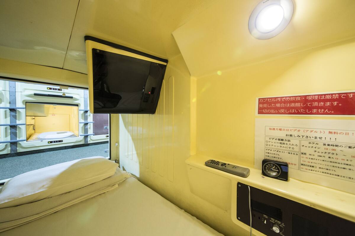 A hotel room with a bed, a television mounted on the wall, a remote control, and a sign with information in Japanese.