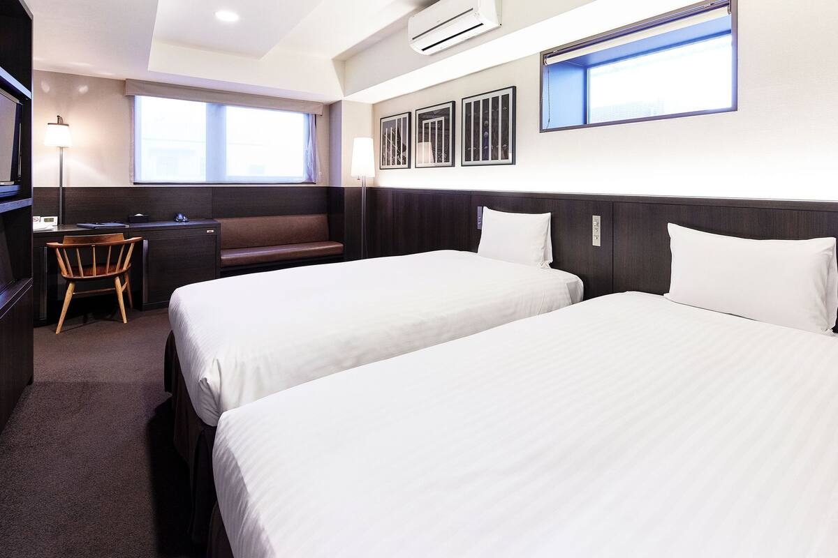 Une chambre d’hôtel avec deux lits, un bureau, une chaise et de grandes fenêtres.