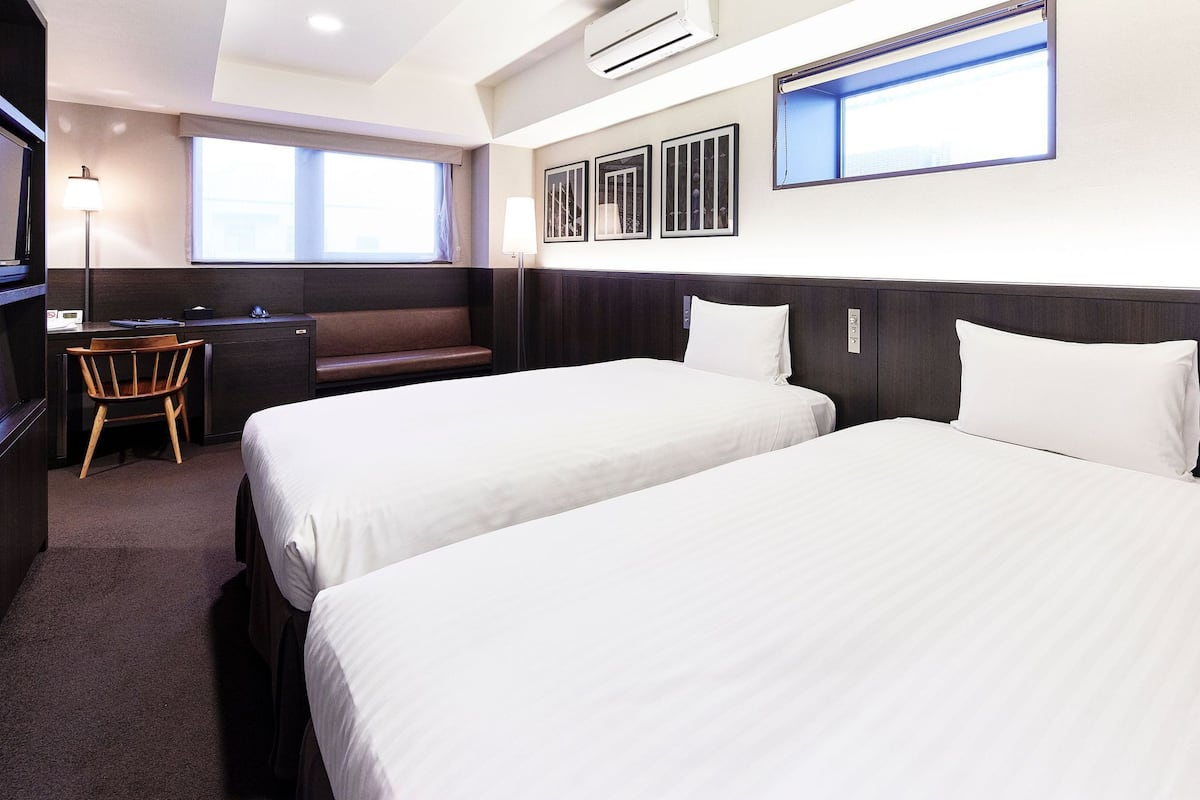 Une chambre d’hôtel avec deux lits, un bureau, une chaise et de grandes fenêtres.