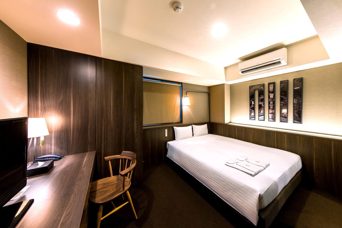Une chambre d’hôtel équipée d’un lit, d’un bureau, d’une chaise et d’un climatiseur fixé au mur.