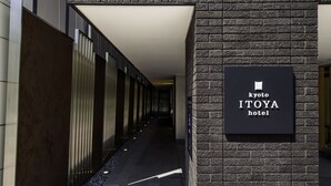 A corridor leading to the Kyoto Itoya Hotel, featuring a modern design with a brick wall and a signboard.