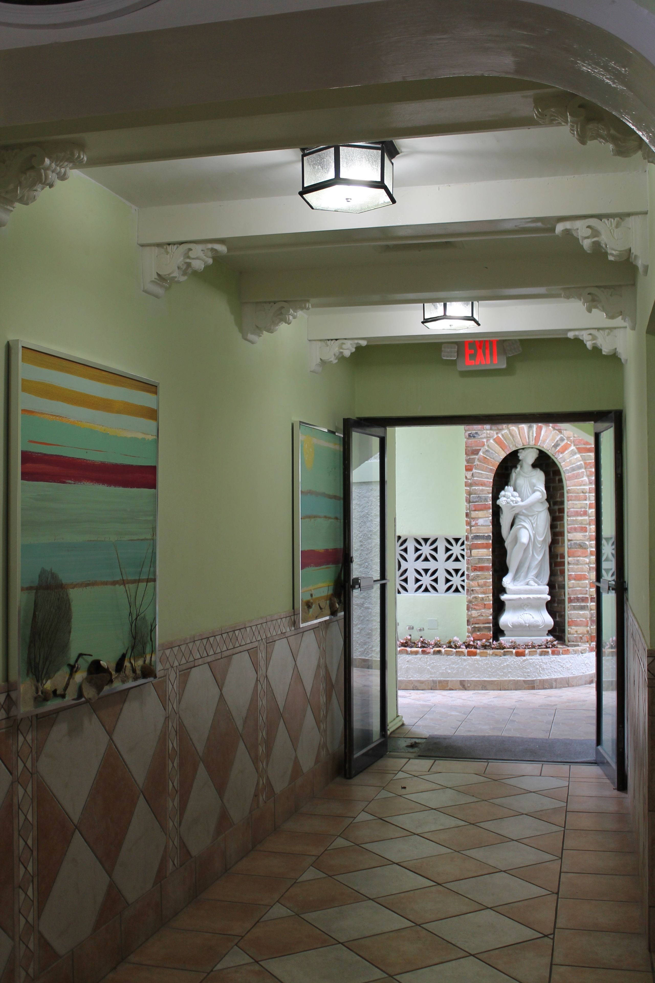 A hallway with a tiled floor, a statue, and a framed painting.