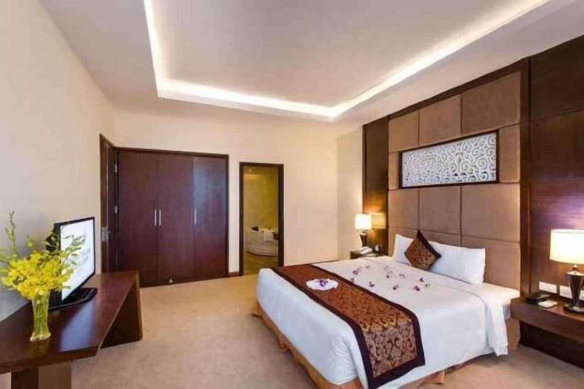 A hotel room with a large bed, bedside tables, a desk, and a wardrobe.