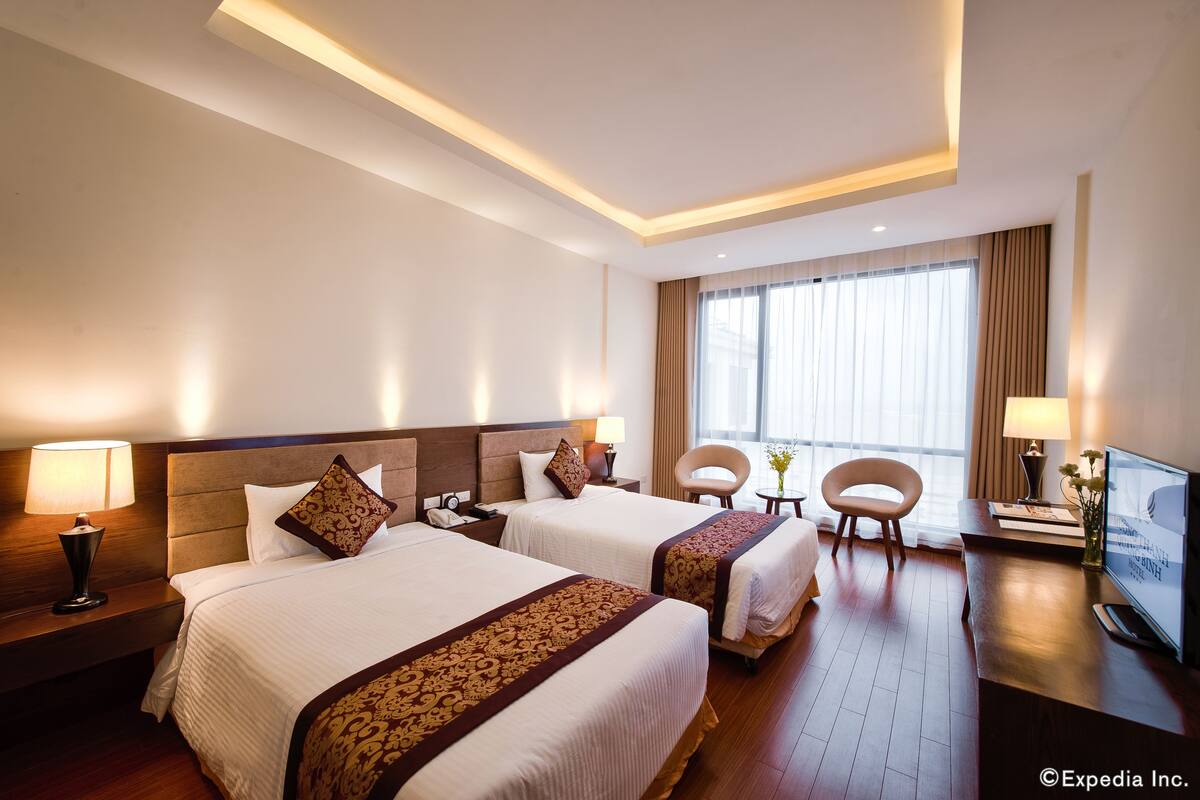 A hotel room with two beds, a desk, a chair, and a television.
