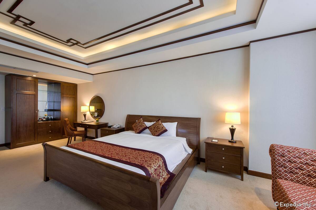 A hotel room with a large bed, wooden headboard, bedside tables with lamps, a desk, and a chair.