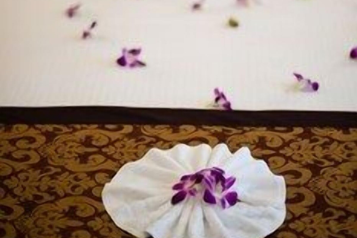 A bed with white linens, a brown pillow, and a decorative white flower on the bedspread.