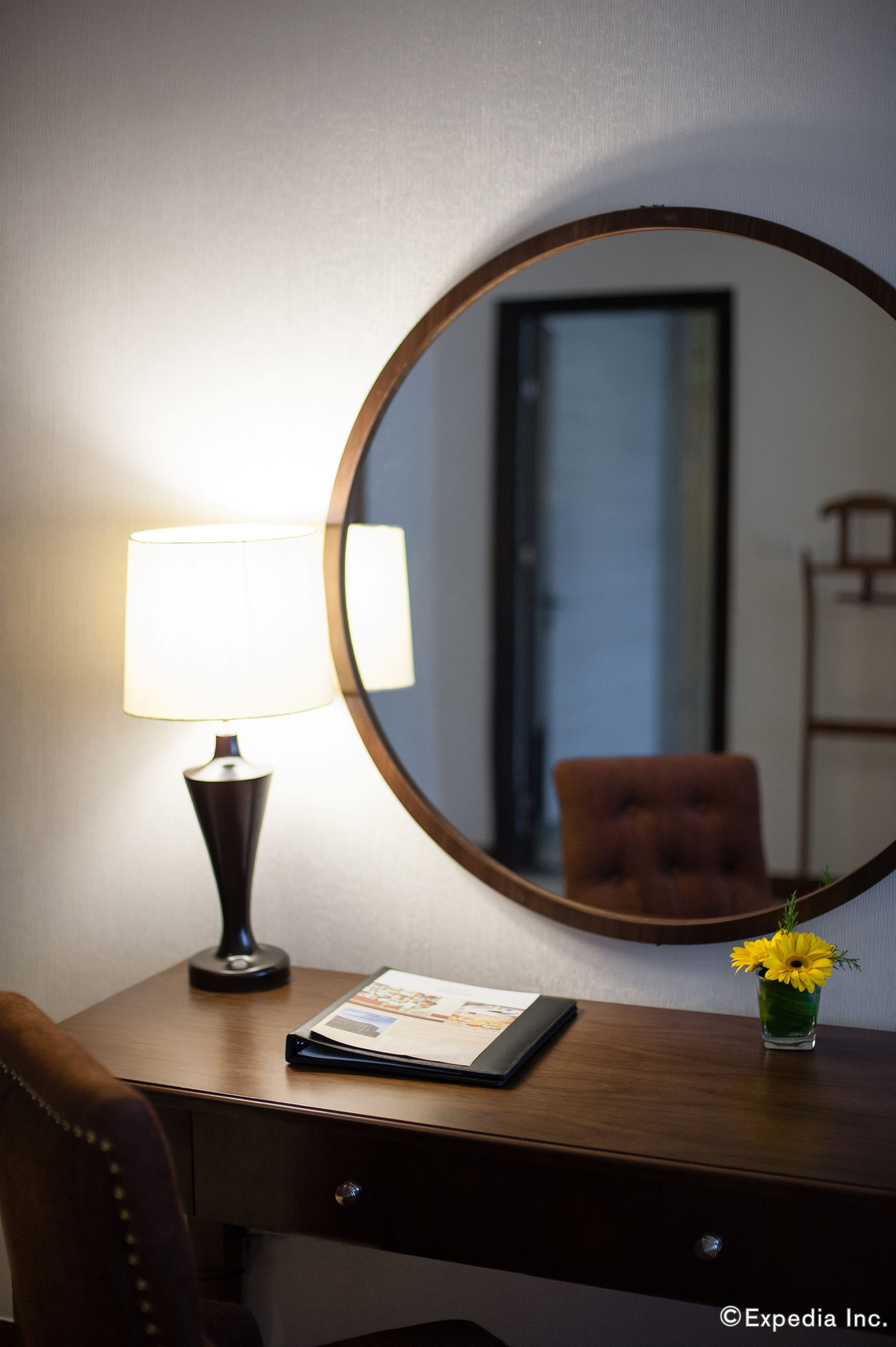 Un bureau avec une lampe, un miroir, un tableau encadré et un vase de fleurs.