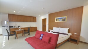 A compact hotel room with a bed, a red sofa, a small table, and a kitchenette. - The Patong Center Hotel (Patong)