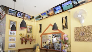 A reception area with a curved wooden counter, multiple pendant lights, a wall-mounted TV display, and a fan. - The Patong Center Hotel (Patong)
