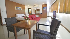 A hotel room with a wooden dining table, wicker chairs, a red sofa, a small TV, and a window with curtains. - The Patong Center Hotel (Patong)