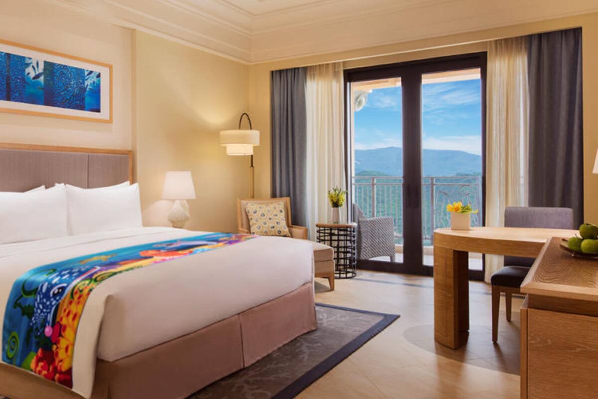 Une chambre d’hôtel avec un grand lit, une table à manger, une chaise, une petite table avec un vase et une vue sur l’extérieur.