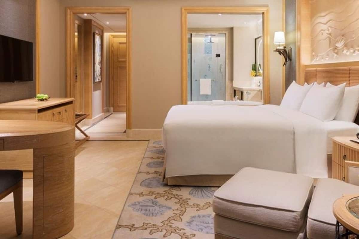 Une chambre d’hôtel avec un lit, un bureau, une chaise, une télévision et une salle de bain visible à travers une porte ouverte.