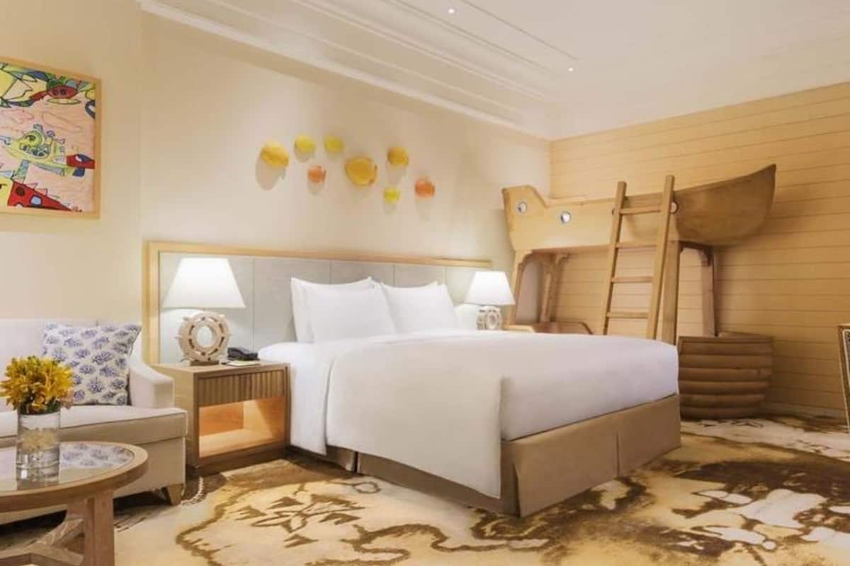 Une chambre d’hôtel avec un grand lit, deux tables de chevet, une lampe, un élément décoratif mural et une échelle en bois.