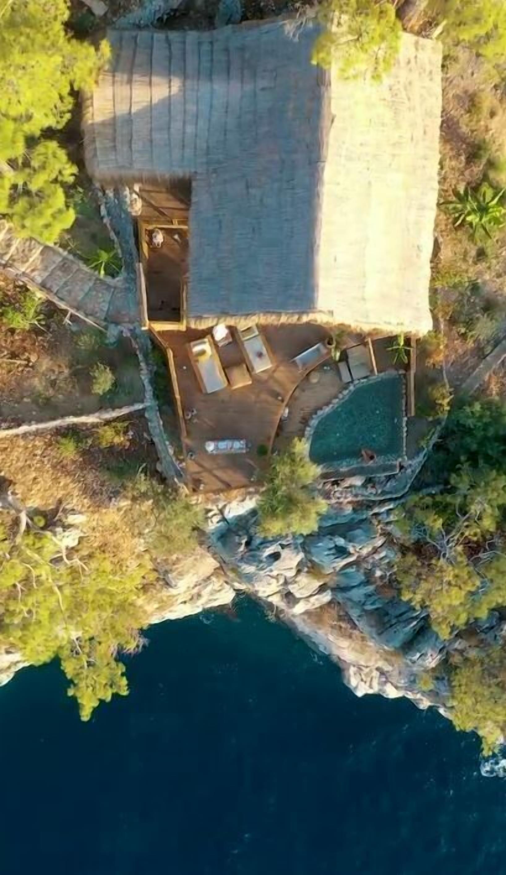 An aerial view of a coastal property with a swimming pool, outdoor seating area, and a small dock.